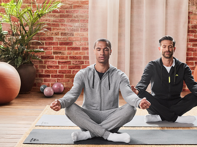 Deux hommes méditant sur des tapis de yoga, vêtus de survêtements.