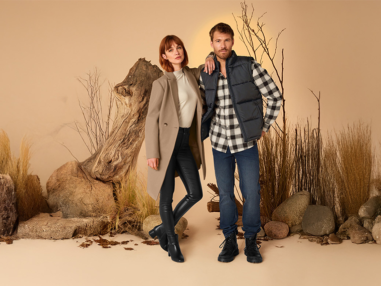 Un homme et une femme posent dans des tenues d'automne décontractées, avec un gilet et un manteau.