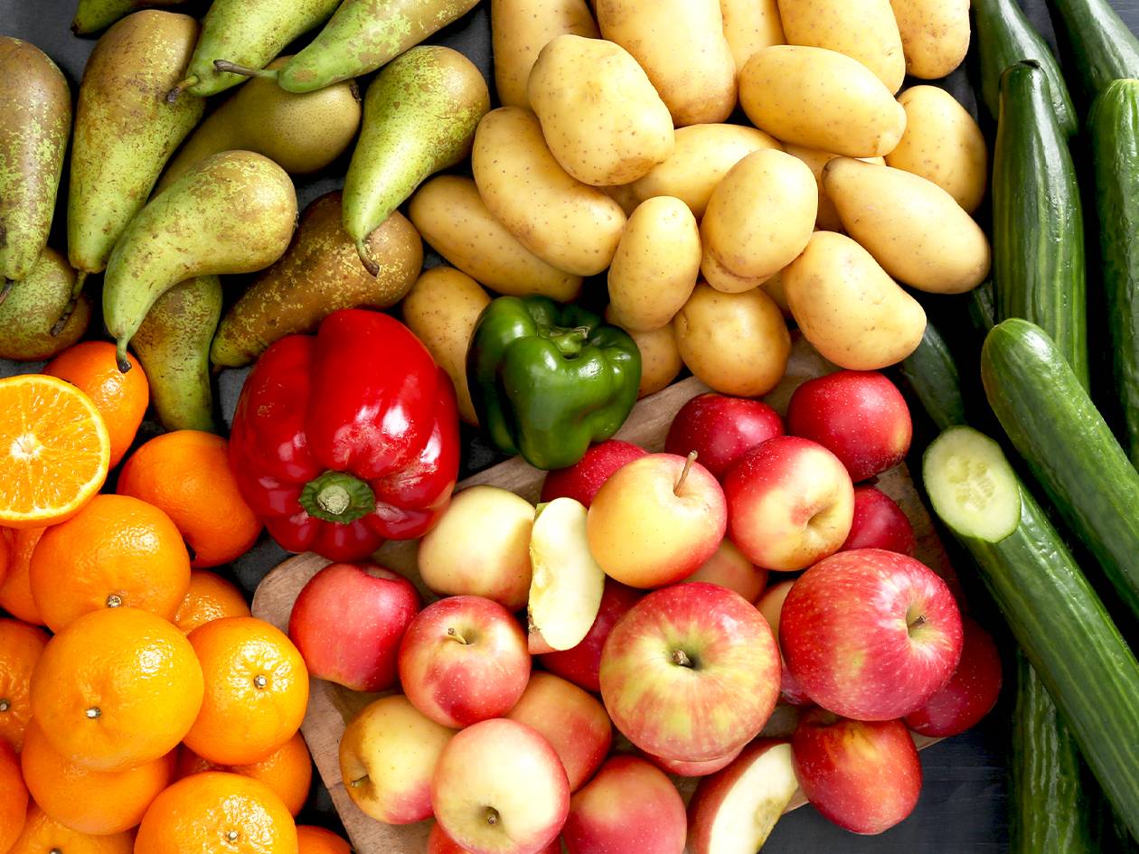 Un assortiment de fruits et légumes frais, notamment des poires, des pommes de terre, des concombres, des oranges, des poivrons et des pommes.