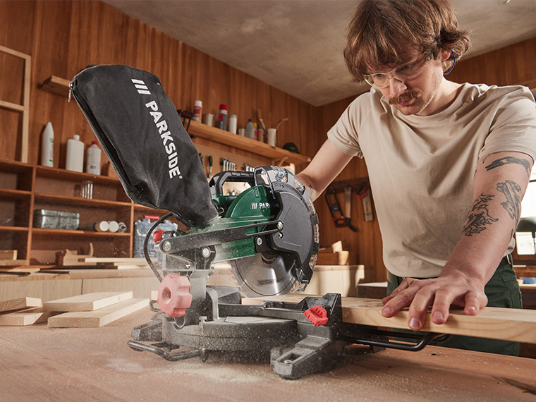 Un homme utilise une scie à onglets Parkside pour couper du bois dans son atelier.