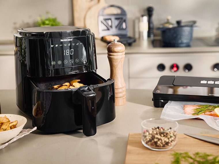 Une friteuse SilverCrest noire avec des pommes de terre à l'intérieur, sur un comptoir de cuisine avec d'autres appareils électroménagers.
