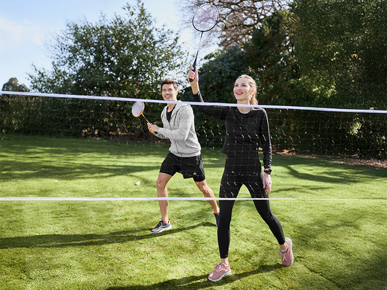 Un couple joue au badminton dans un jardin ensoleillé.