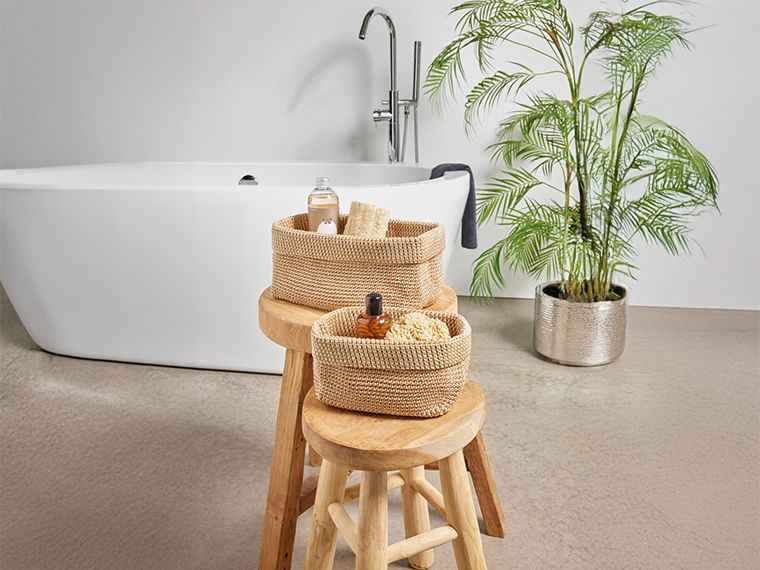 Baignoire blanche avec robinet, deux tabourets en bois et des paniers de rangement tressés.