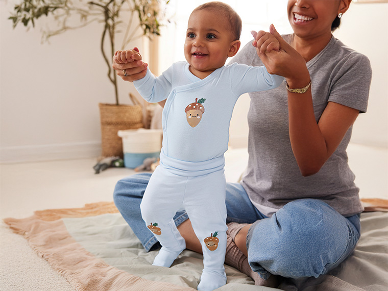 Un bébé adorable portant une grenouillère en coton bio à motif glands, tenu par sa mère.