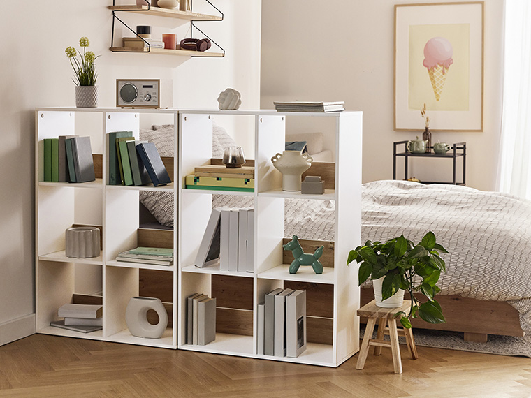 Deux étagères blanches divisent une chambre à coucher, créant un espace de rangement et une séparation visuelle.