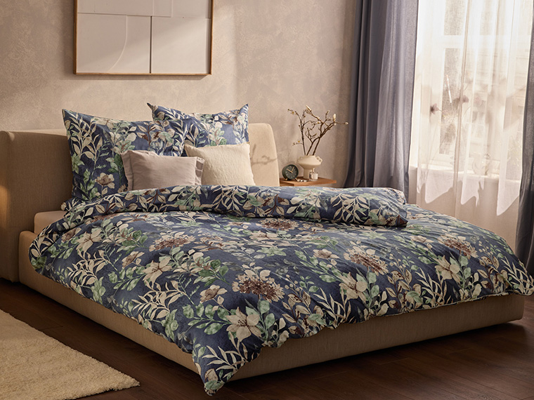 Une chambre avec un lit beige et une parure de lit florale bleue, verte et blanche.