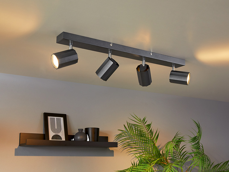 Un plafonnier noir à quatre spots au-dessus d'une étagère avec des décorations et une plante.