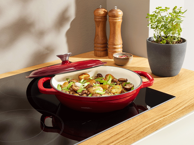 Cocotte rouge avec pommes de terre et champignons sur une plaque de cuisson à induction.