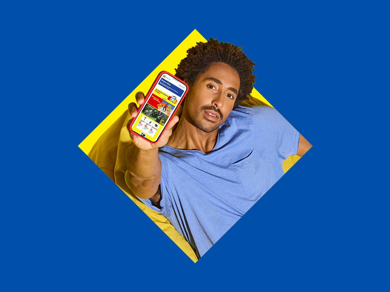 Homme souriant tenant un smartphone affichant des offres sur des outils et des articles de jardinage.