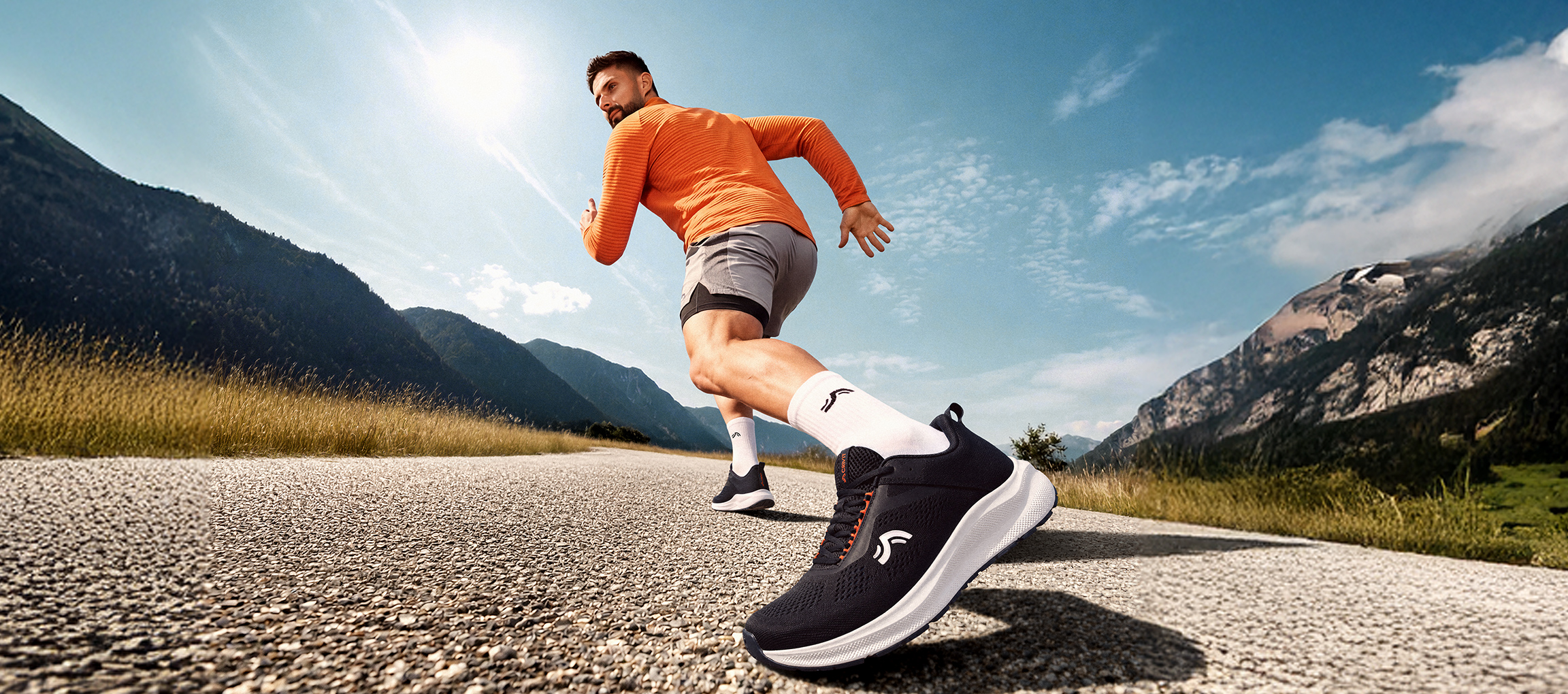 Un homme court sur une route de montagne, portant des chaussures de sport noires et un haut de course orange.