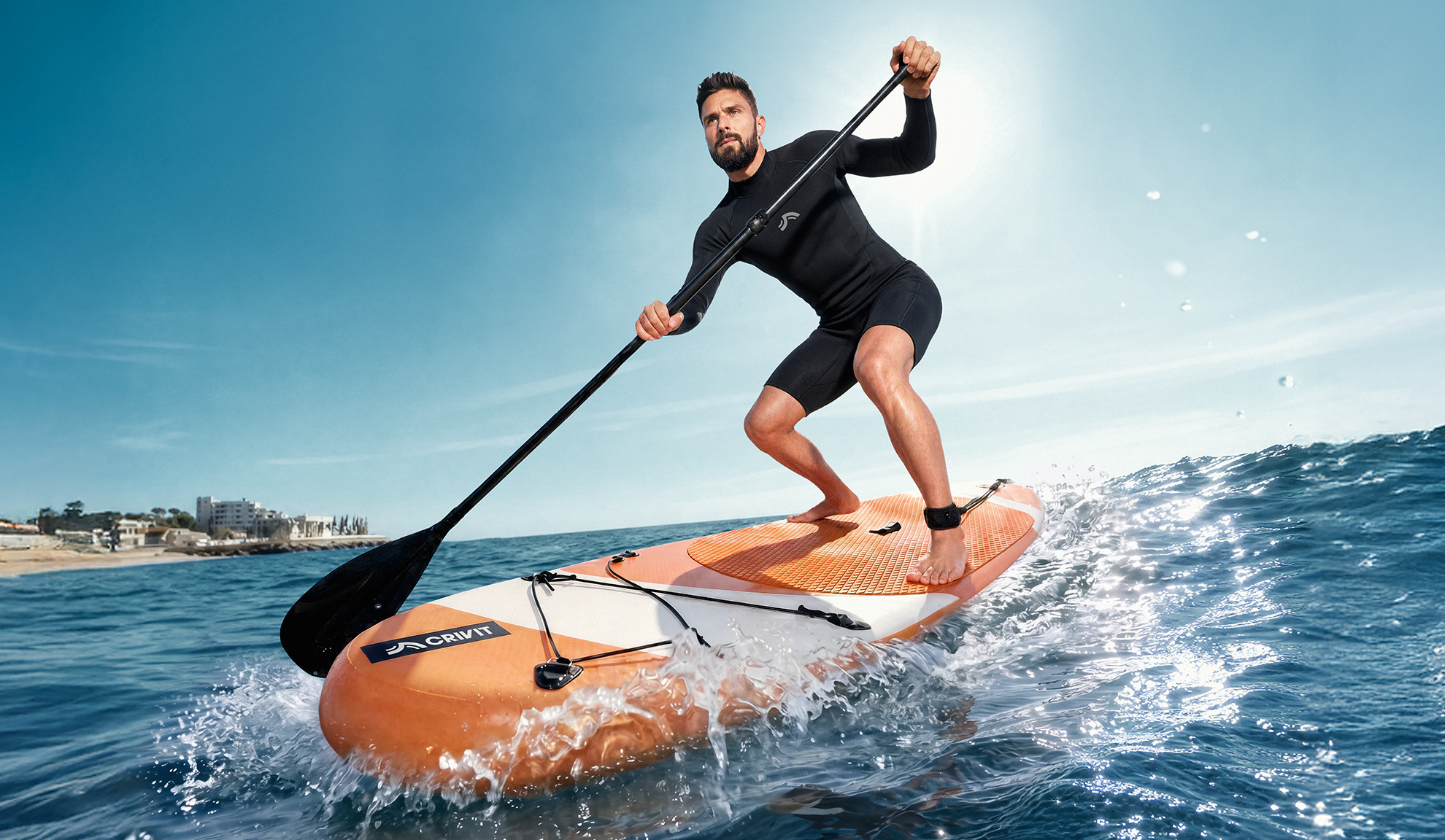 Homme en combinaison de plongée faisant du stand up paddle sur l'eau.