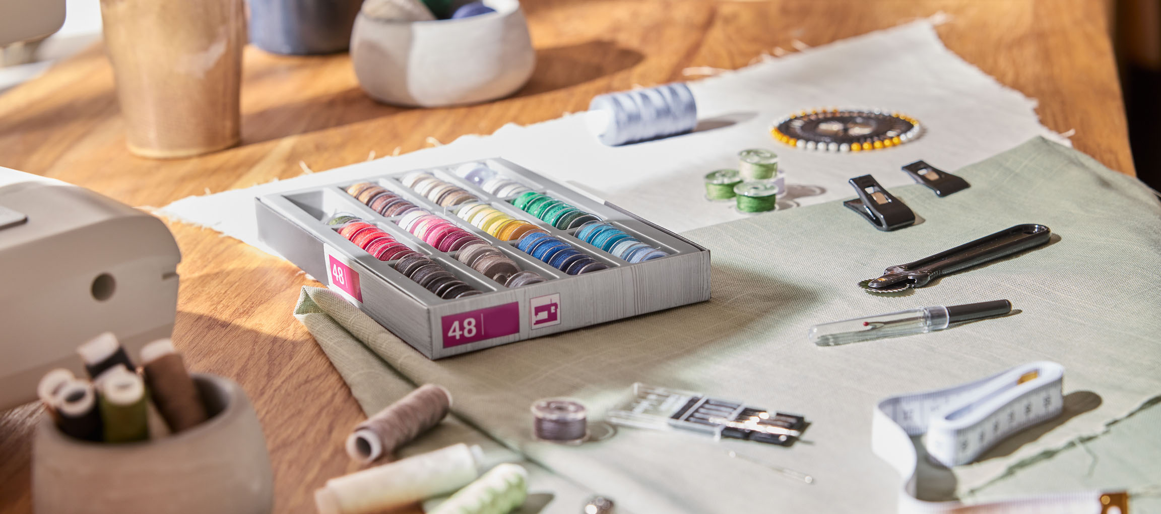 Fournitures de couture sur une table en bois, y compris un organisateur de fils avec 48 bobines, tissu et divers outils.