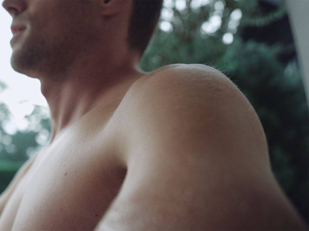 Gros plan sur l'épaule et le cou d'un homme, avec un arrière-plan vert flou.