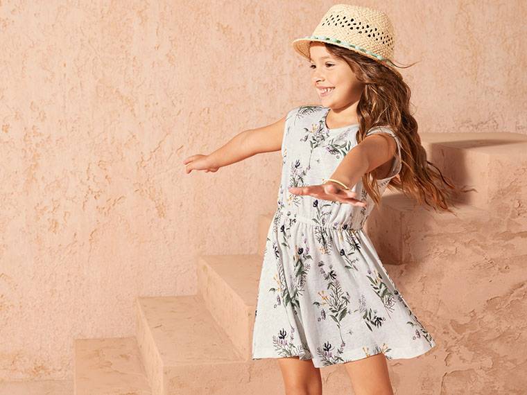 Une jeune fille porte une jolie robe fleurie et un chapeau de paille.