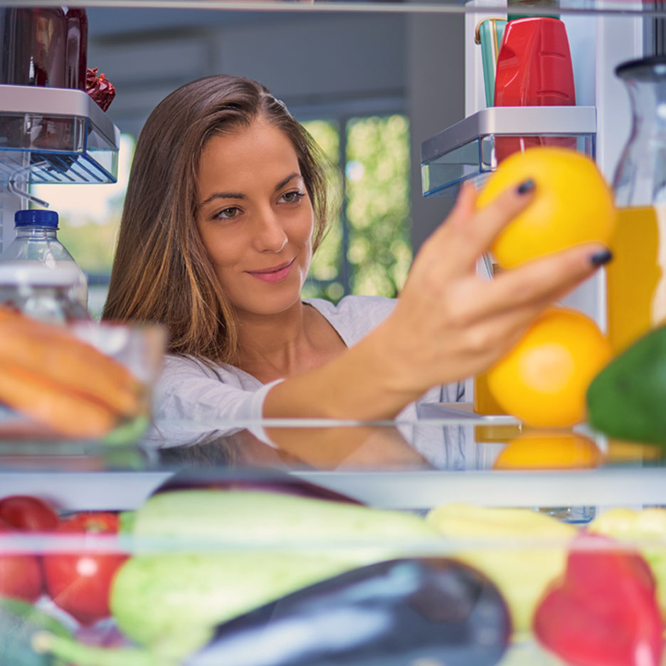 Une femme prend des oranges dans le réfrigérateur.
