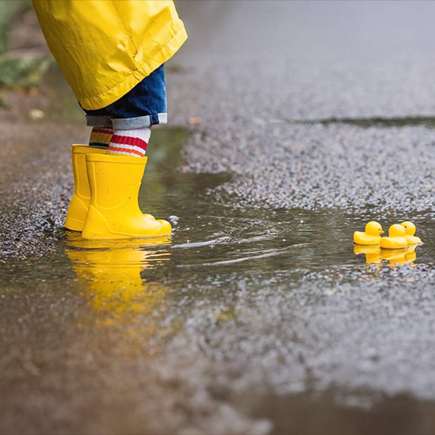 Enfant en bottes de pluie jaunes et imperméable dans une flaque avec des canards en caoutchouc.