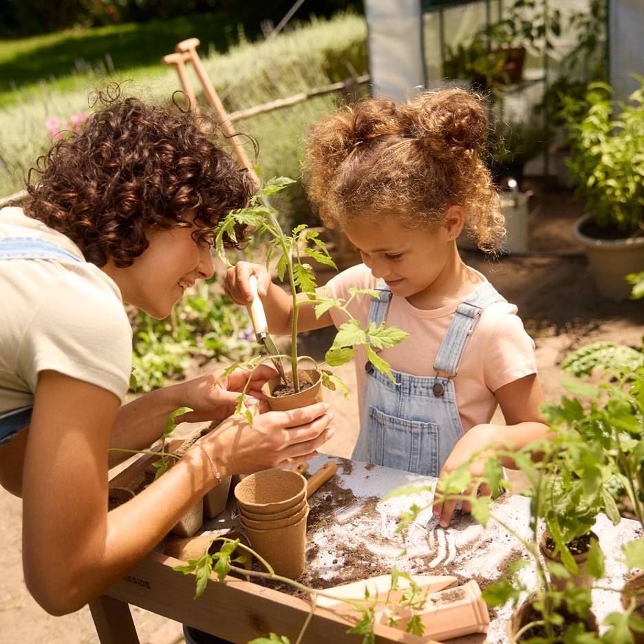 Mère et enfant plantant des semis dans des pots biodégradables, entourés d'outils de jardinage.
