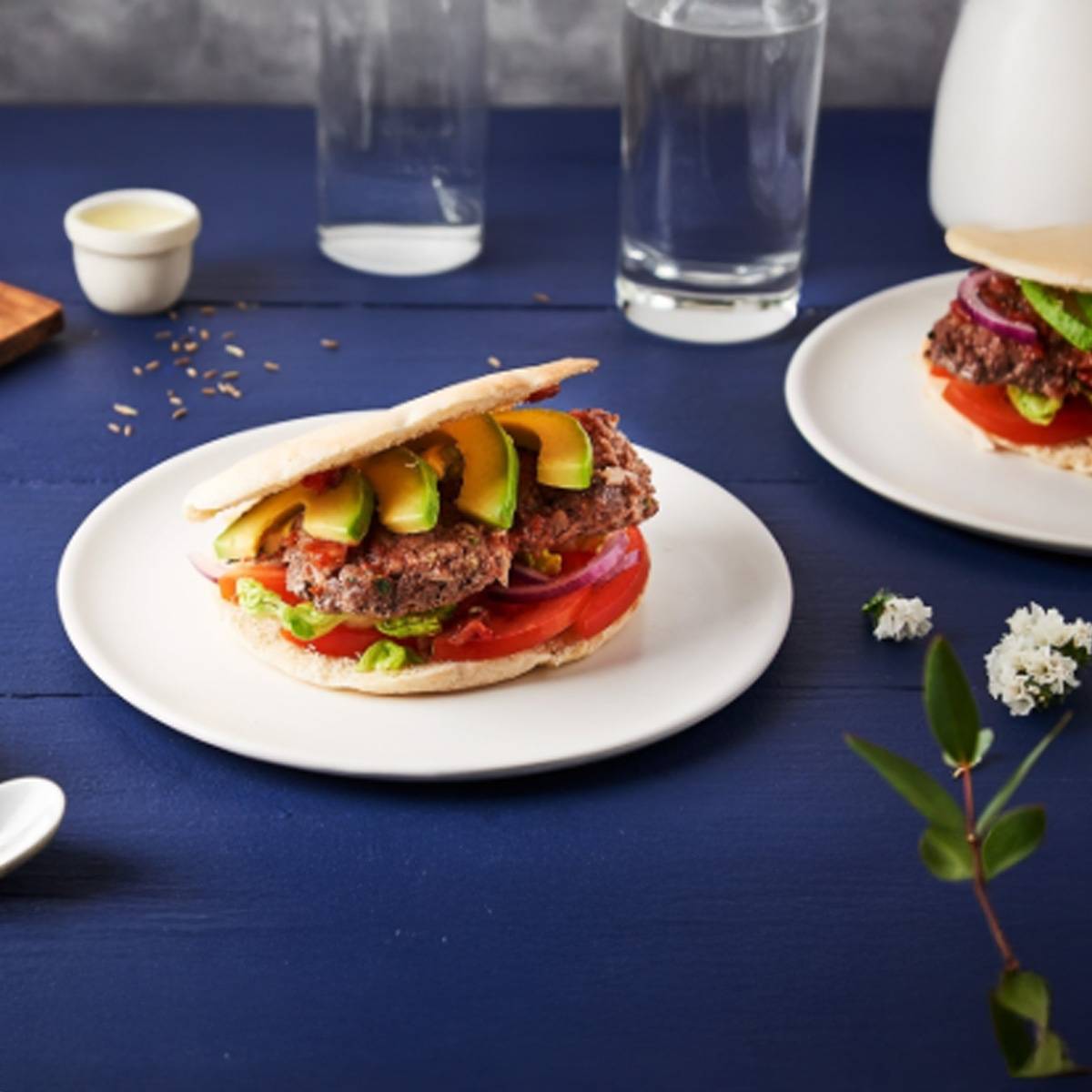 Deux burgers végétariens garnis d'avocat sont présentés sur des assiettes blanches.