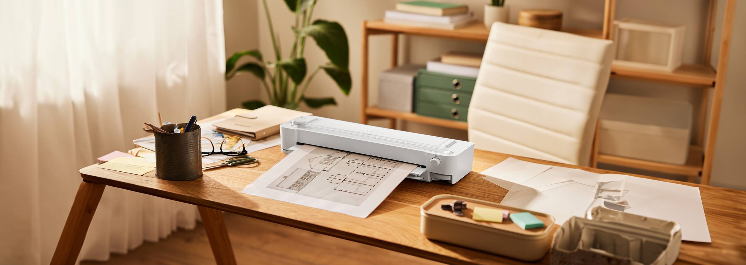 Une imprimante compacte blanche imprime un plan d'architecte sur un bureau en bois.