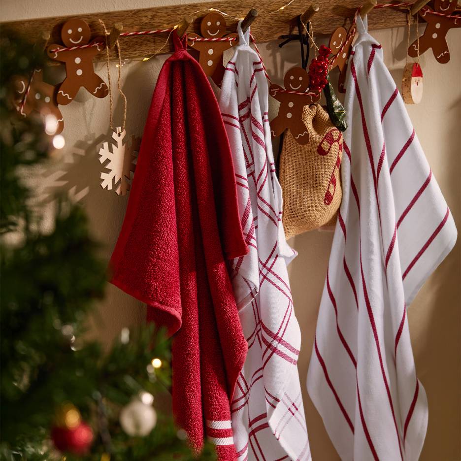 Torchons de cuisine de Noël rouges et blancs suspendus à un porte-serviettes en bois avec des décorations en pain d'épices.