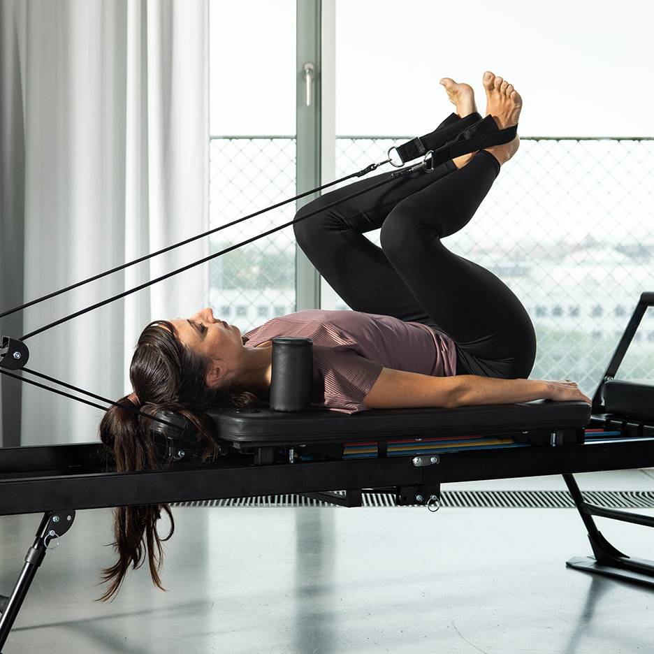 Femme faisant des exercices de jambes sur un reformer Pilates avec des bandes de résistance.