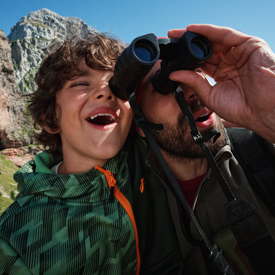 Père et fils explorant les montagnes avec des jumelles, vêtus de vestes d'extérieur.