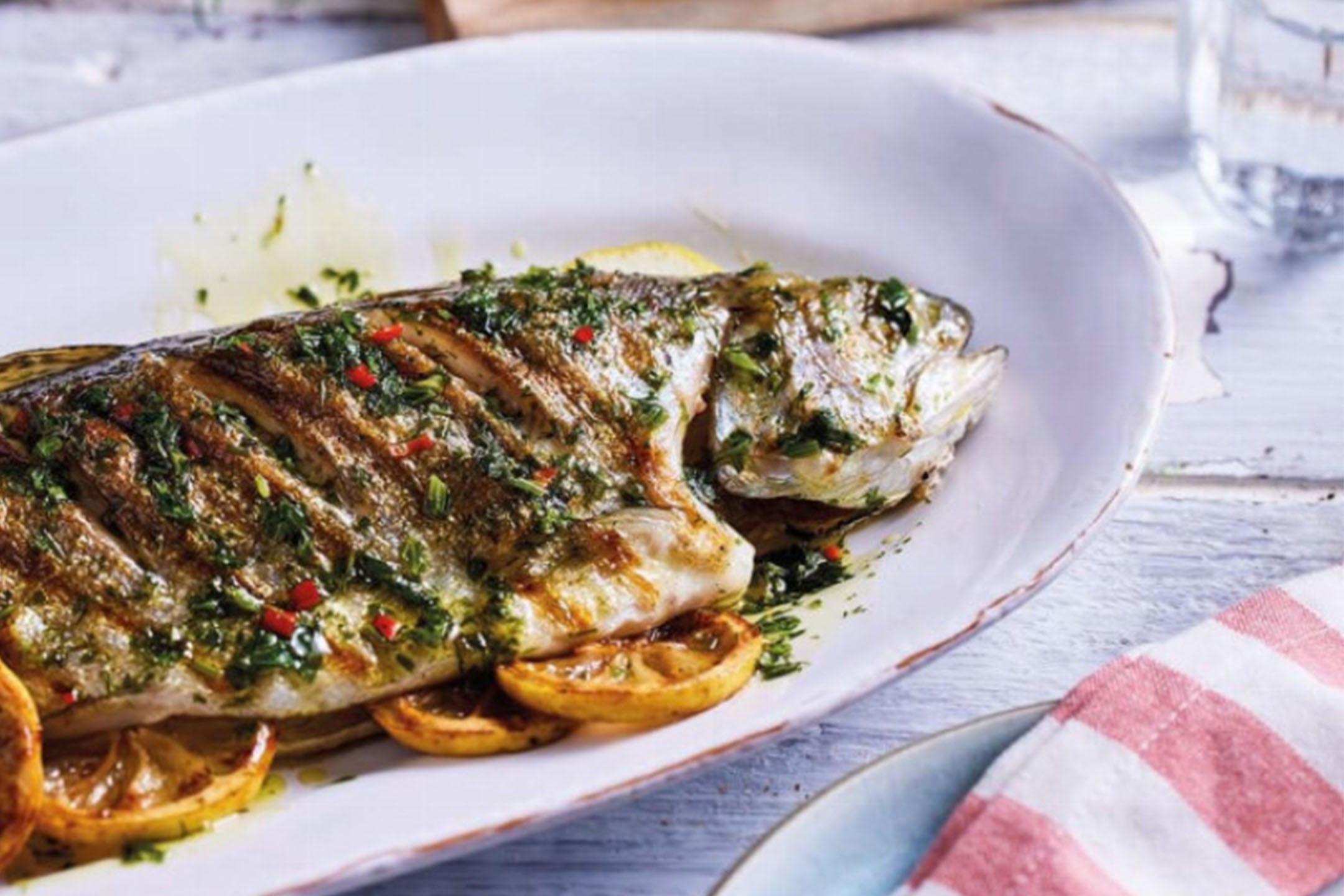 Poisson entier grillé aux herbes et au citron sur un plat blanc.
