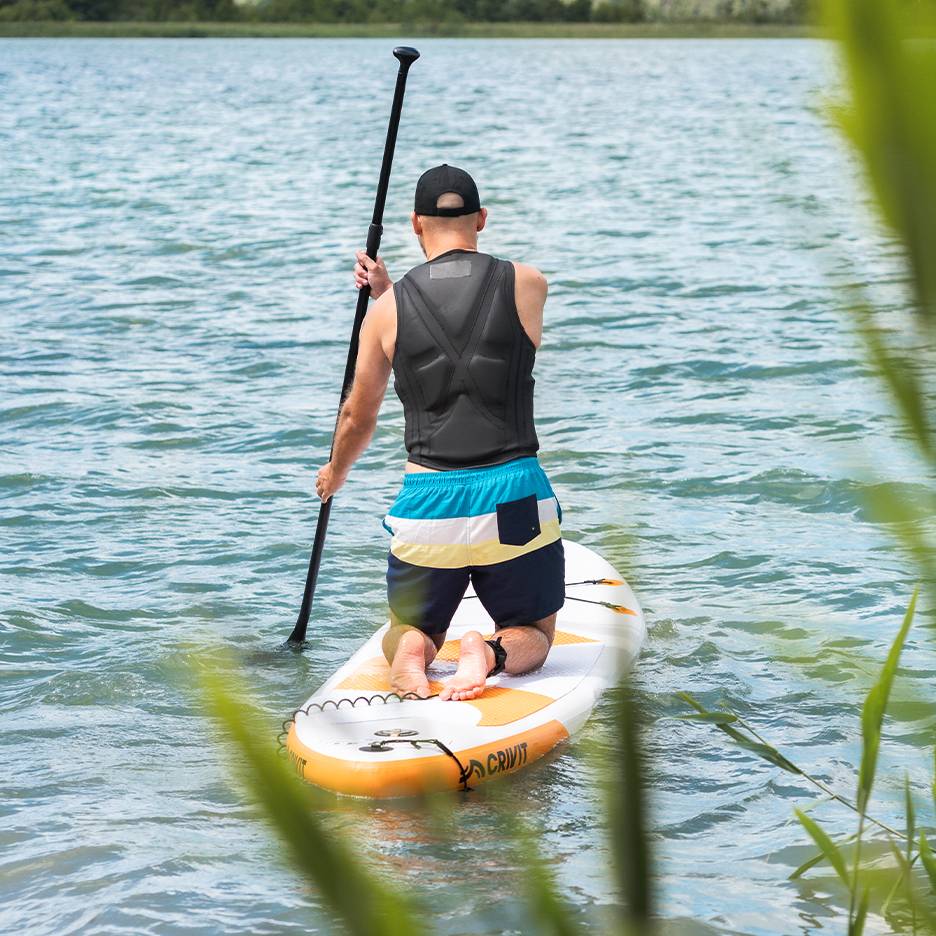Homme pagayant sur un lac sur une planche de SUP Crivit, avec gilet de sauvetage et short de bain.