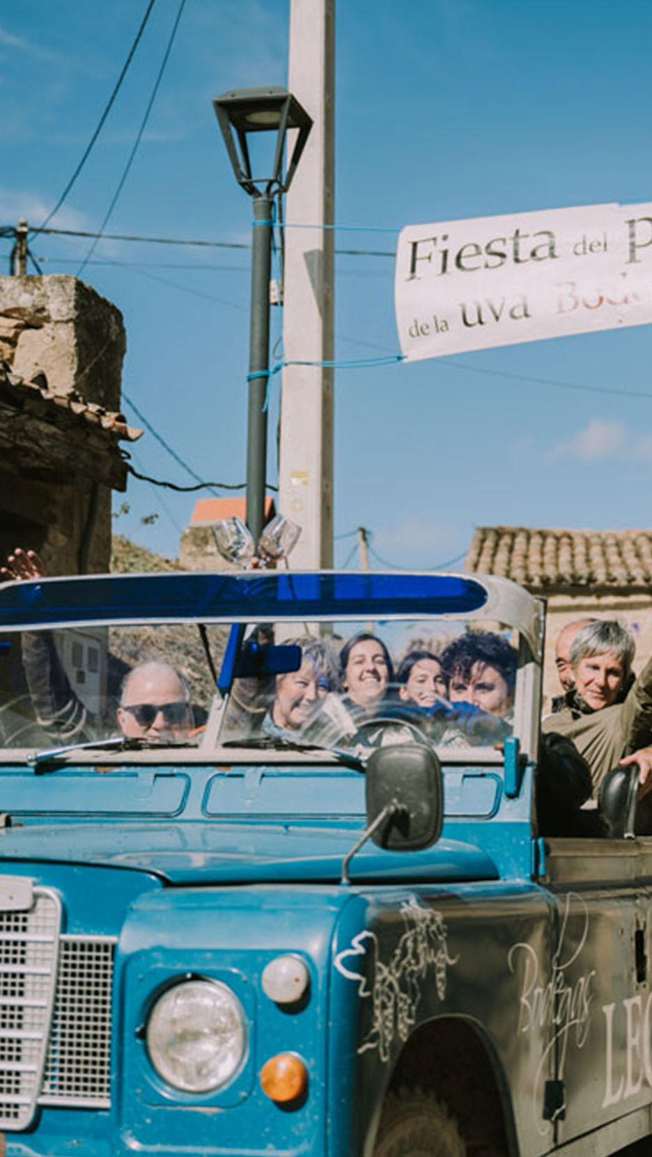 Des gens dans une voiture bleue sous une bannière indiquant 'Fiesta del P de la uva Bod'.