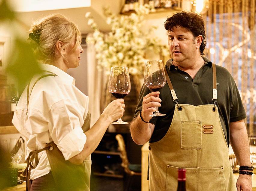 Deux personnes dégustent du vin rouge, vêtues de tabliers.