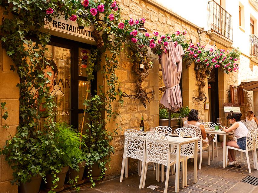 Des gens assis à des tables devant un restaurant avec des fleurs et des plantes grimpantes.