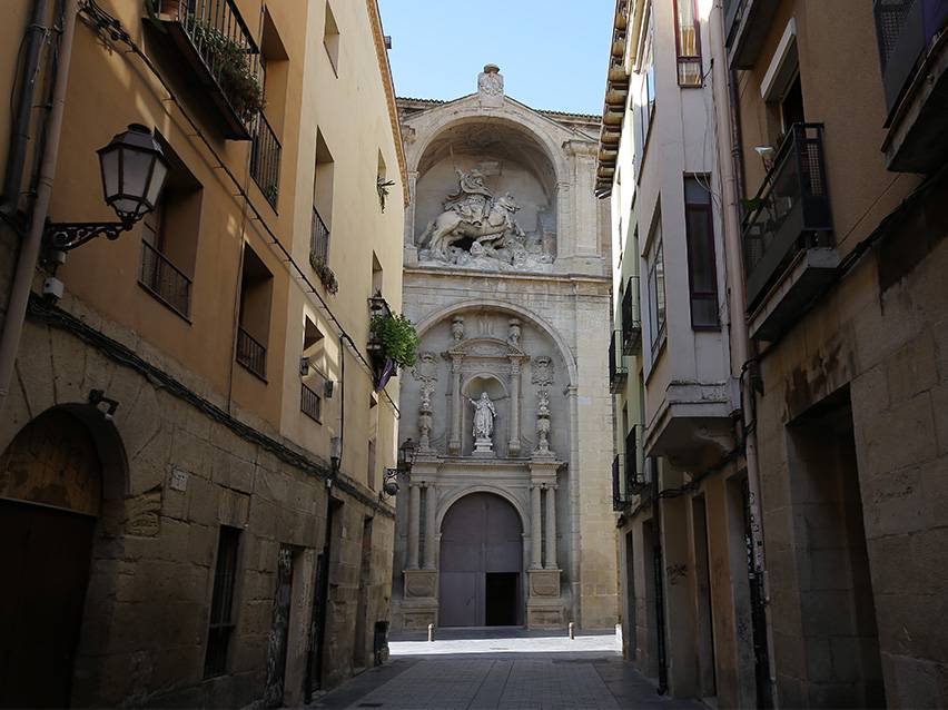 Rue étroite menant à une façade d'église richement décorée avec une statue équestre.