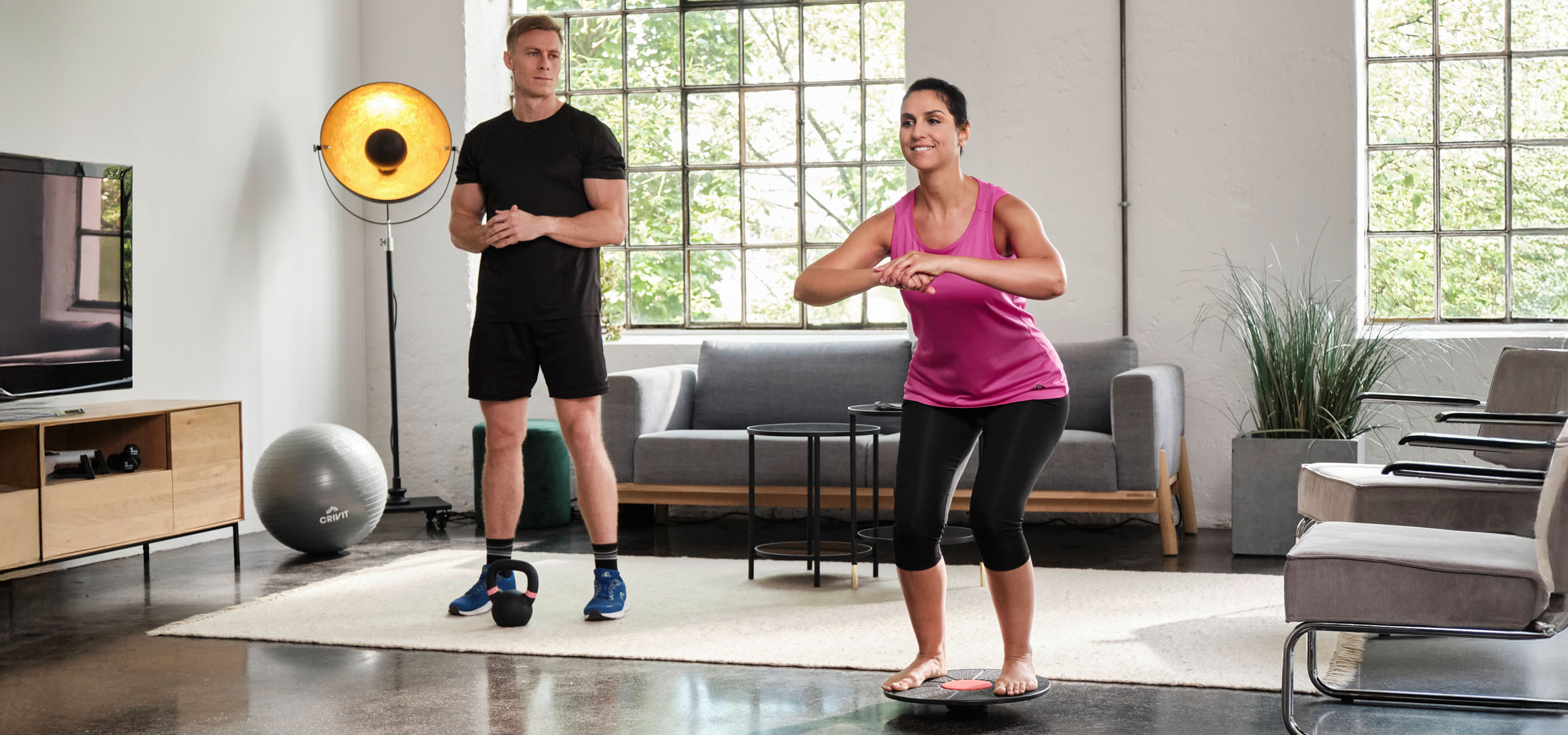 Femme et homme faisant de l'exercice à la maison avec une planche d'équilibre et une kettlebell.