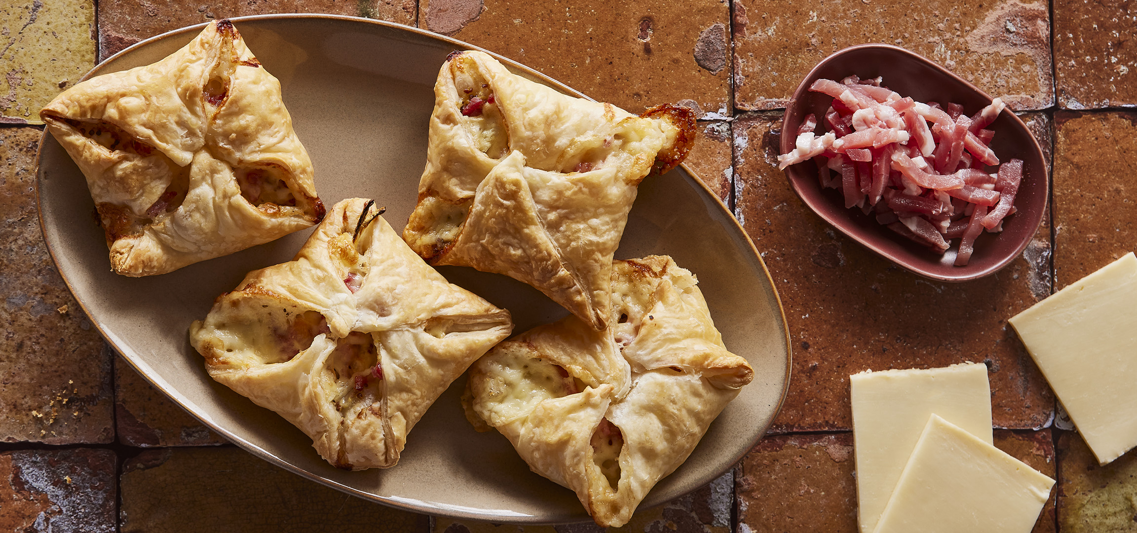 Feuilletés au jambon et fromage, oignon et lardons sur une planche en bois.