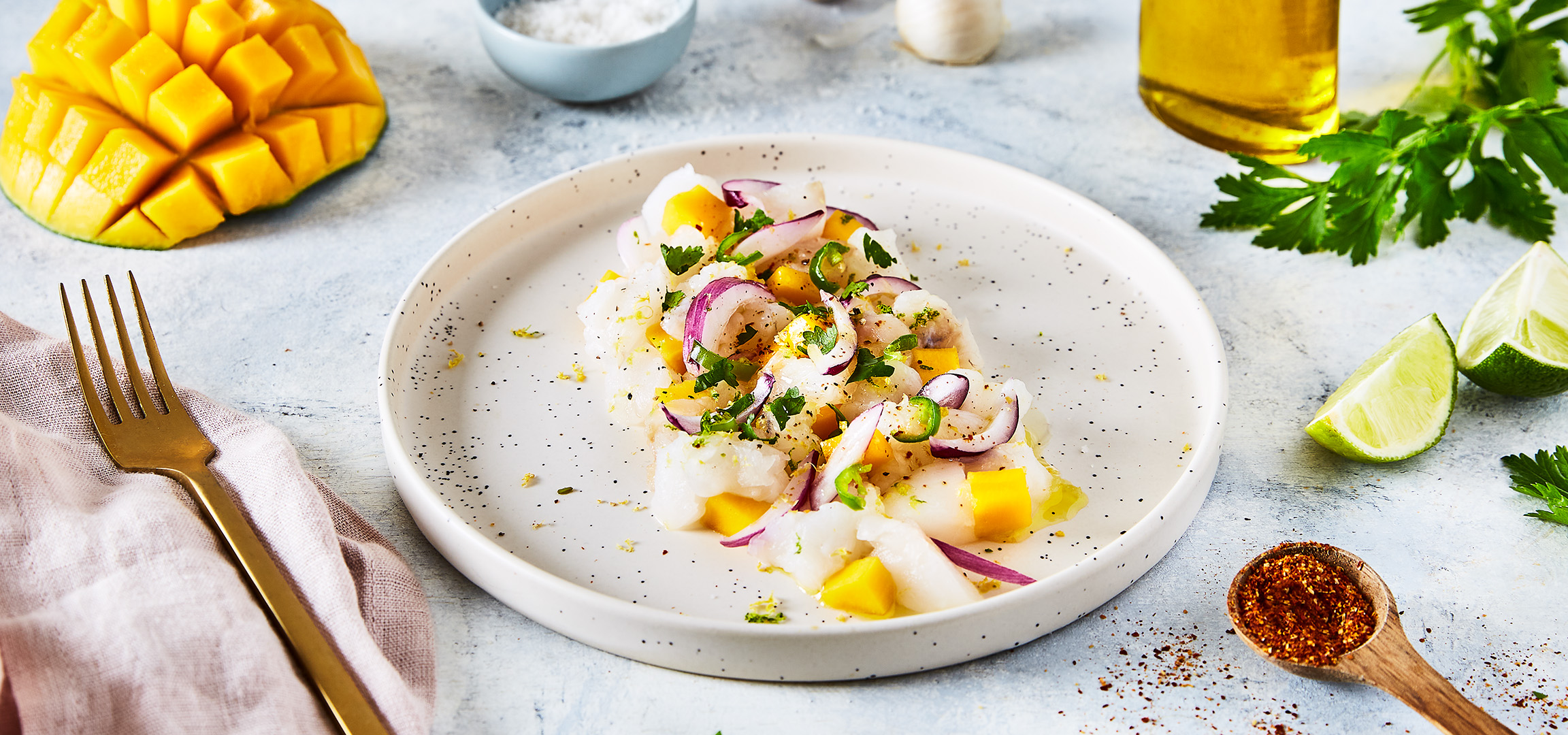 Ceviche de poisson blanc avec mangue, oignon rouge, piment et coriandre sur une assiette blanche.