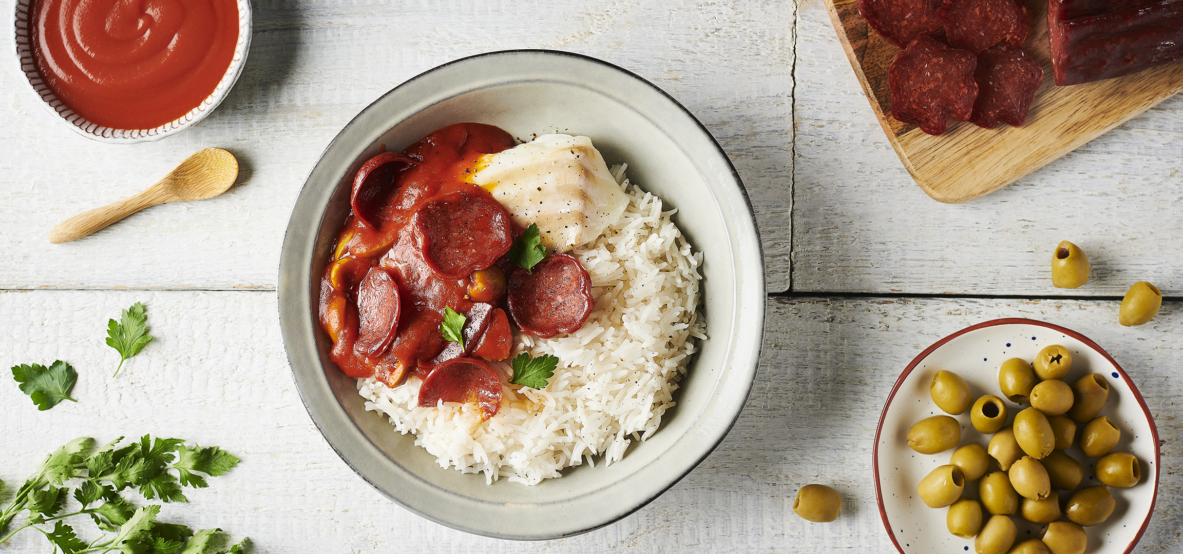 Un plat de riz avec du chorizo et un œuf, accompagné d'olives et de sauce tomate.