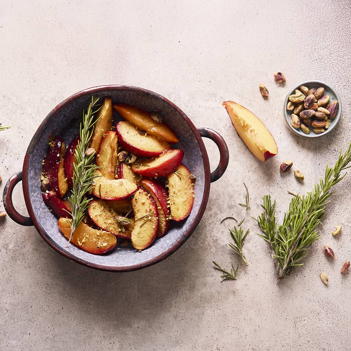 Tranches de nectarines rôties avec du romarin et des pistaches dans un plat en céramique.