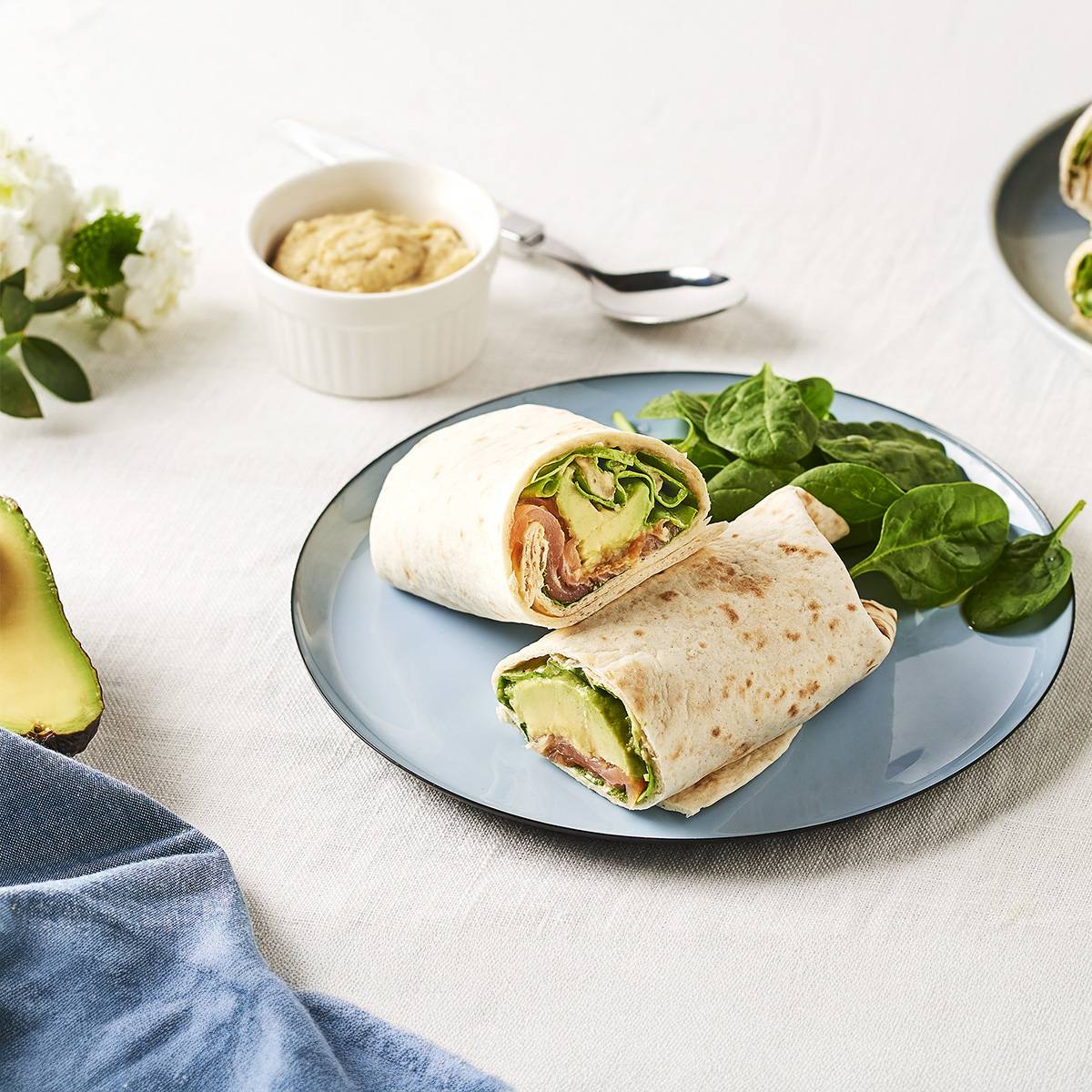 Deux wraps au saumon, avocat et épinards, servis avec une sauce et une portion d'avocat.