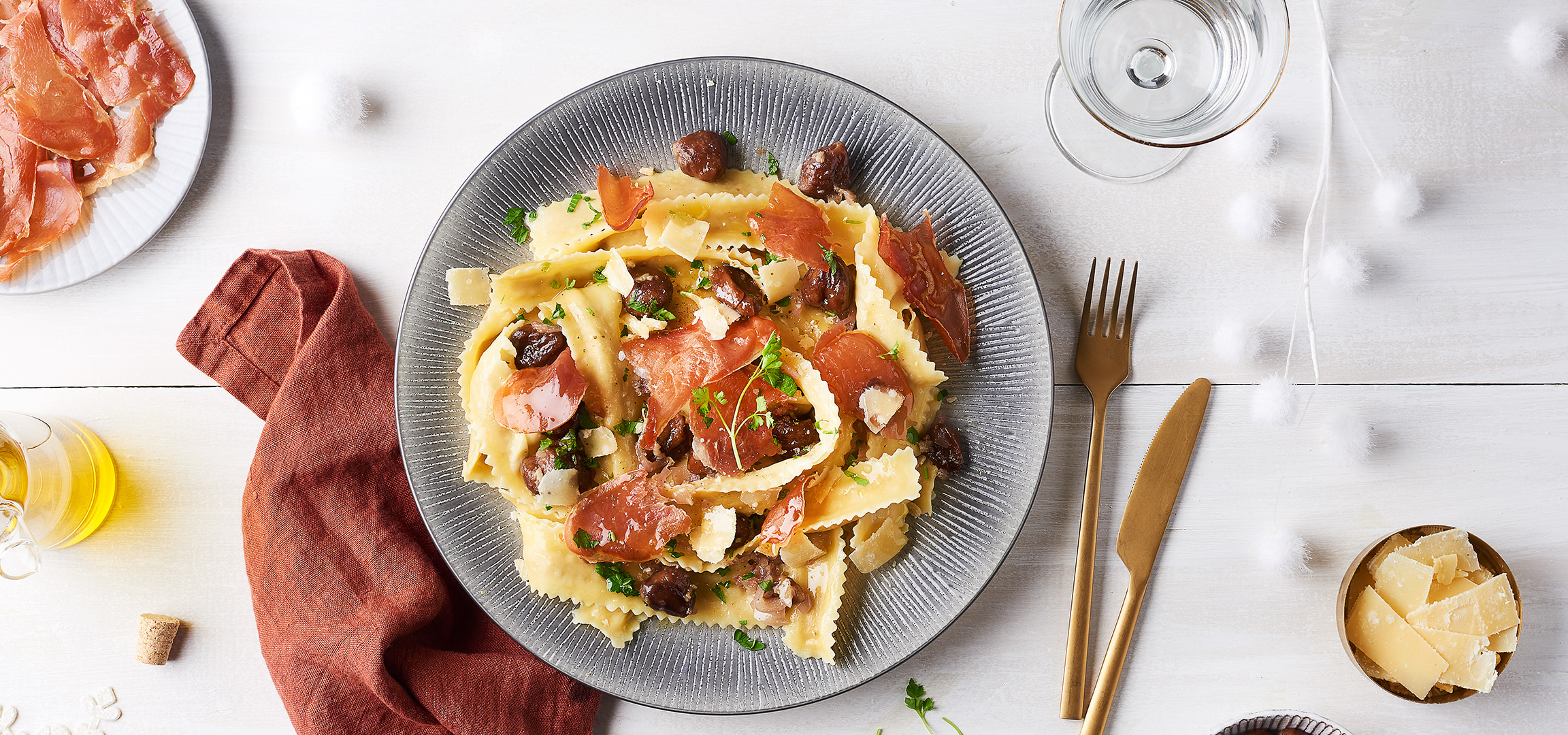 Pâtes aux champignons, jambon cru et parmesan sur une table en bois blanc.