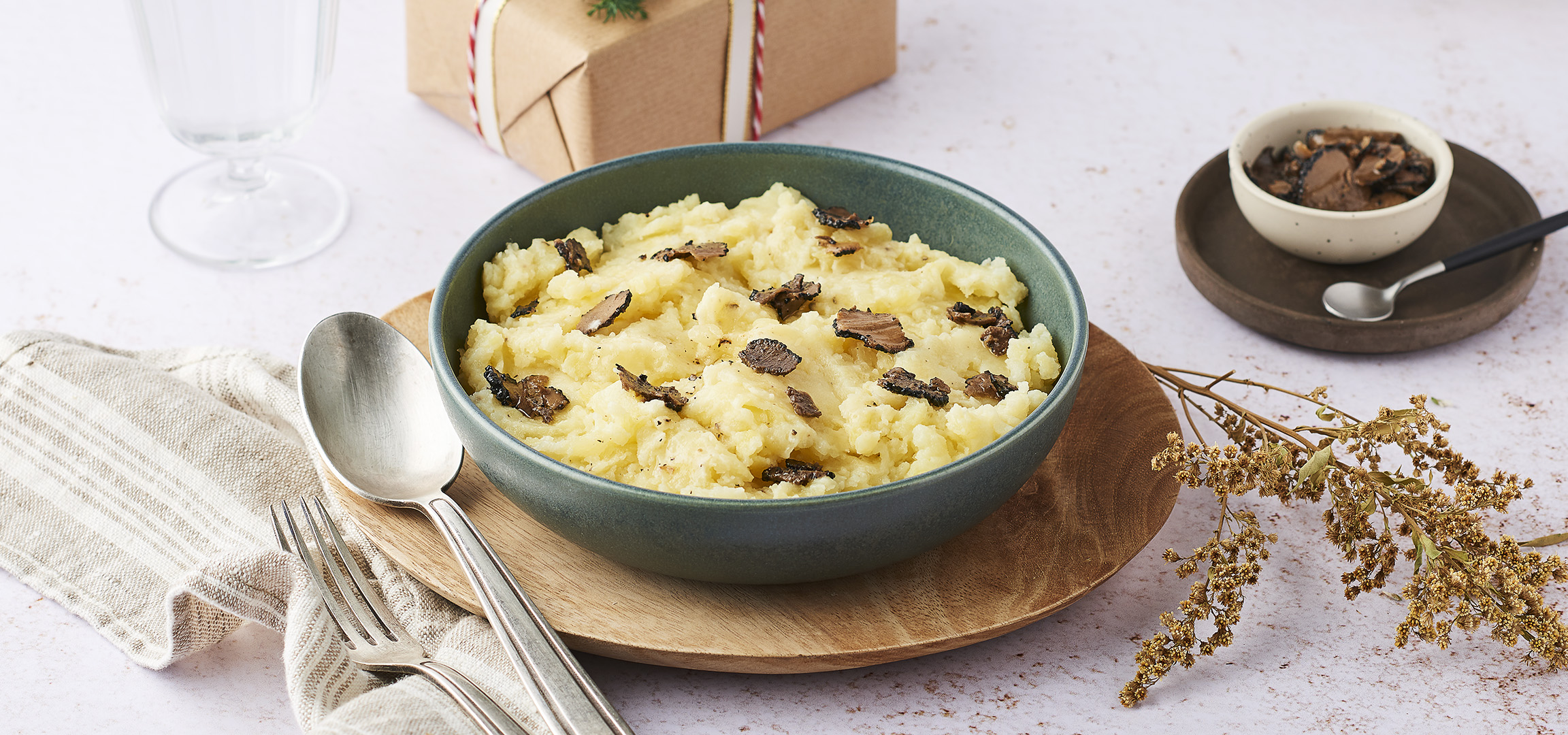 Purée de pommes de terre à la truffe dans un bol vert, avec des couverts et des herbes séchées.