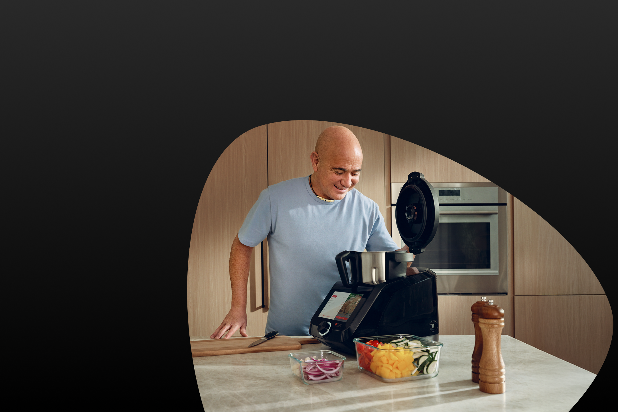 Homme cuisinant dans une cuisine avec un robot culinaire et des légumes coupés.