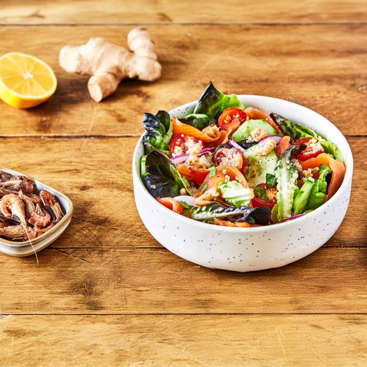 Salade de saumon et quinoa dans un bol blanc, accompagnée de crevettes et de gingembre.