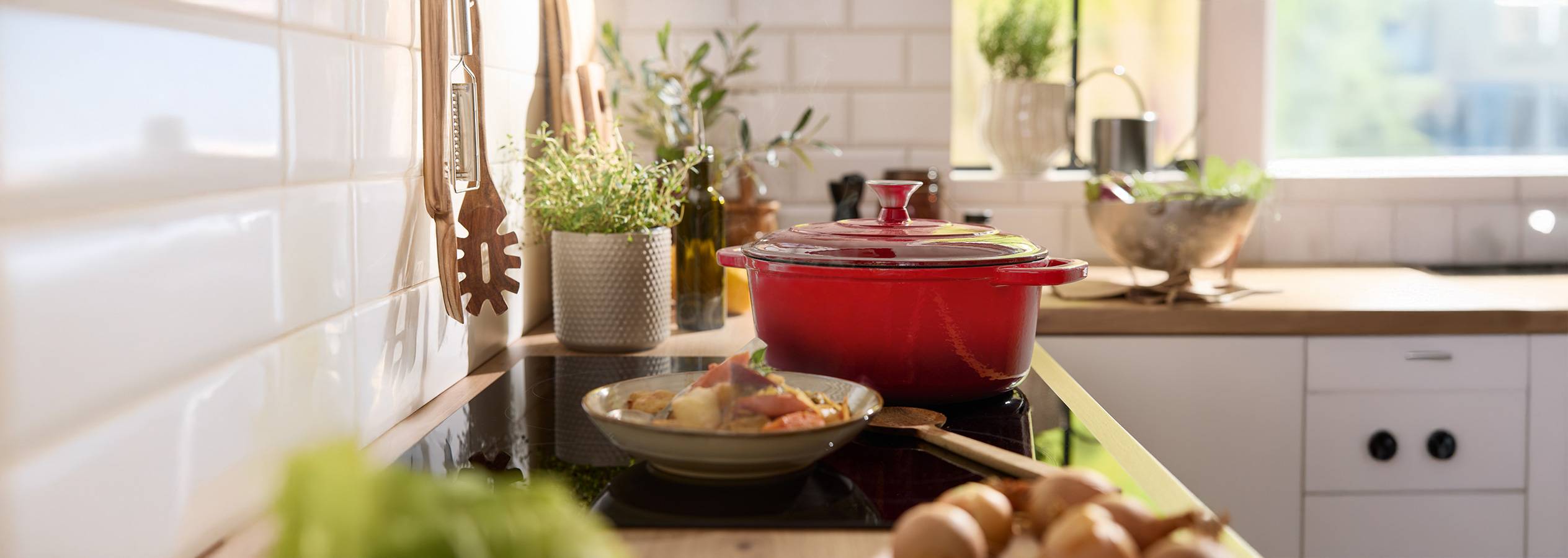 Une cocotte rouge sur une plaque de cuisson avec un plat préparé et des ustensiles de cuisine.