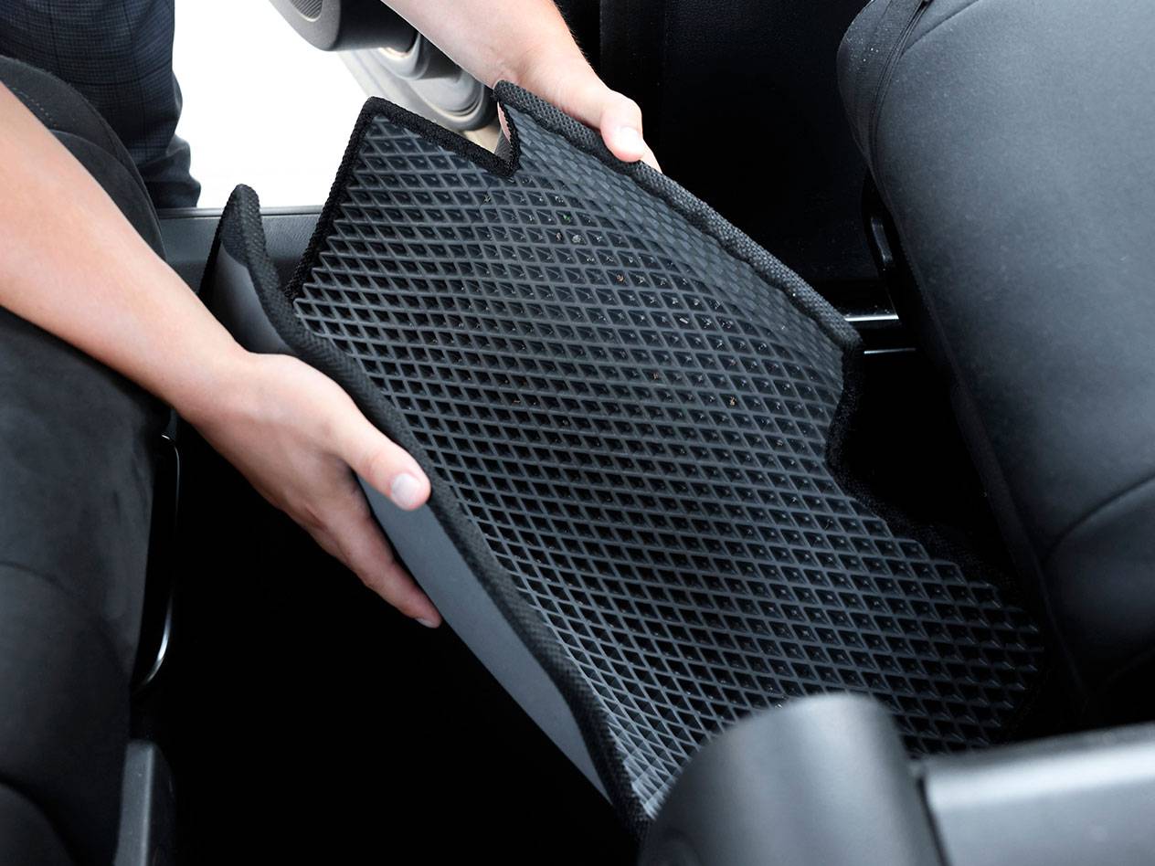 Personne plaçant un tapis de voiture en caoutchouc noir à motif de losanges dans un véhicule.