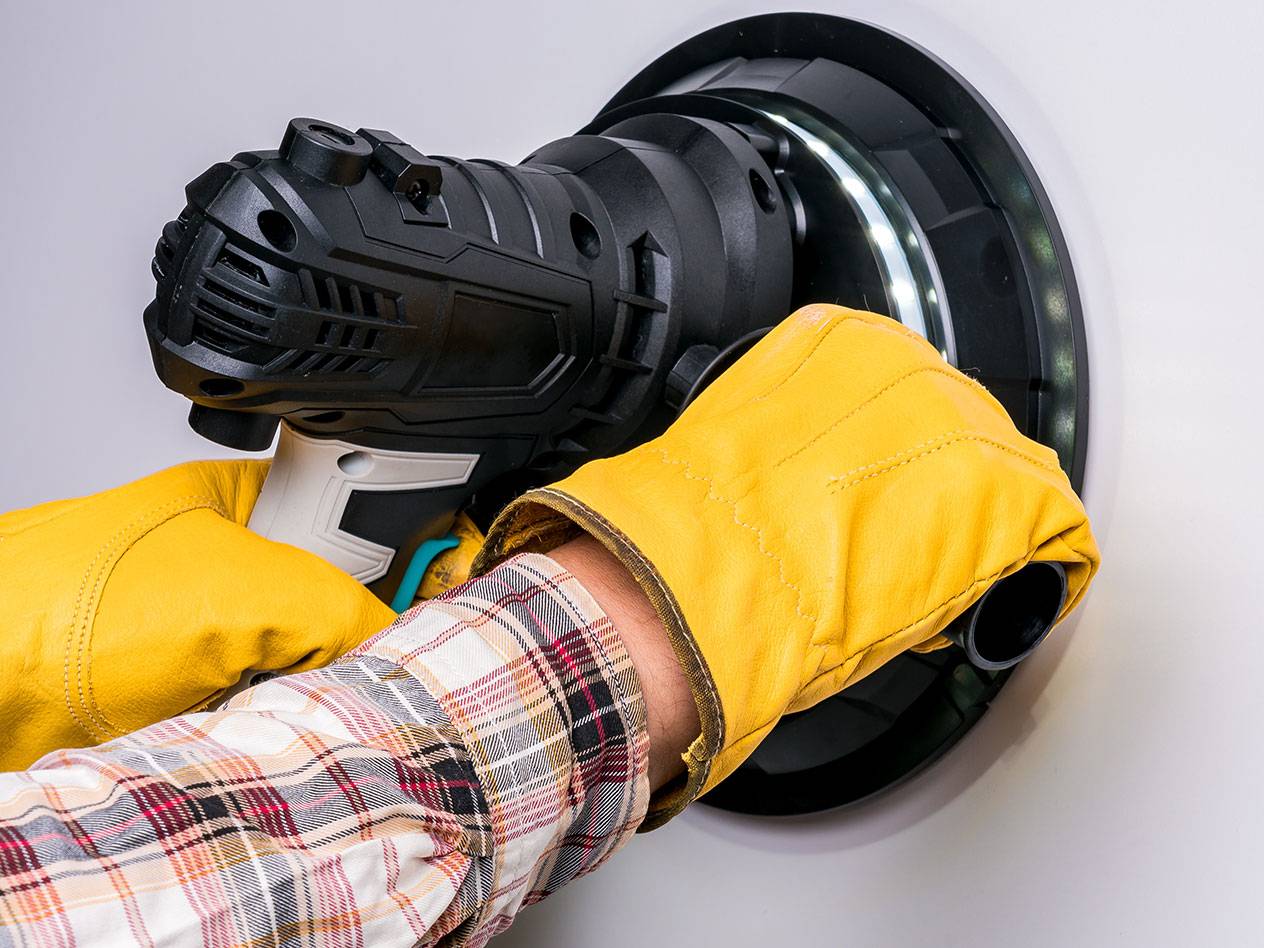 Ponceuse murale électrique avec éclairage LED, utilisée par une personne portant des gants.