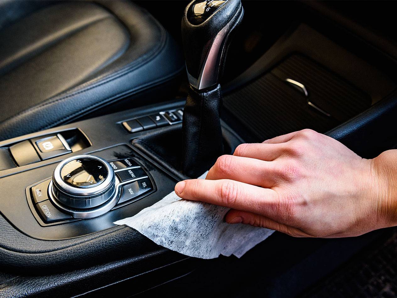 Main nettoyant l'intérieur d'une voiture avec une lingette humide.