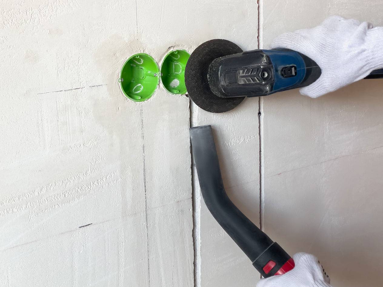 Outil électrique coupant des rainures dans un mur avec un aspirateur pour la poussière.