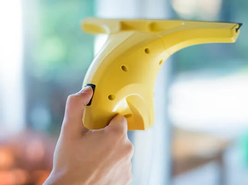 Main tenant un nettoyeur de vitres électrique jaune, nettoyant une fenêtre.