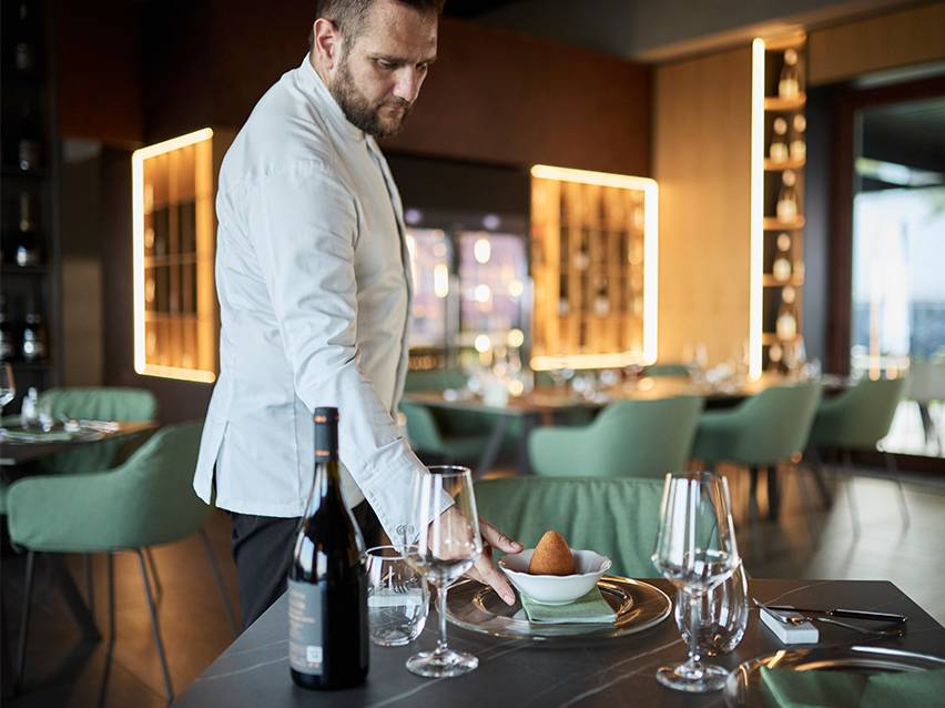 Un chef sert un arancino sur une assiette dans un restaurant.