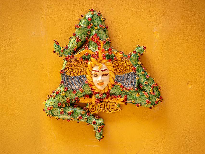 Décoration murale sicilienne en céramique représentant la Trinacria sur un mur jaune.